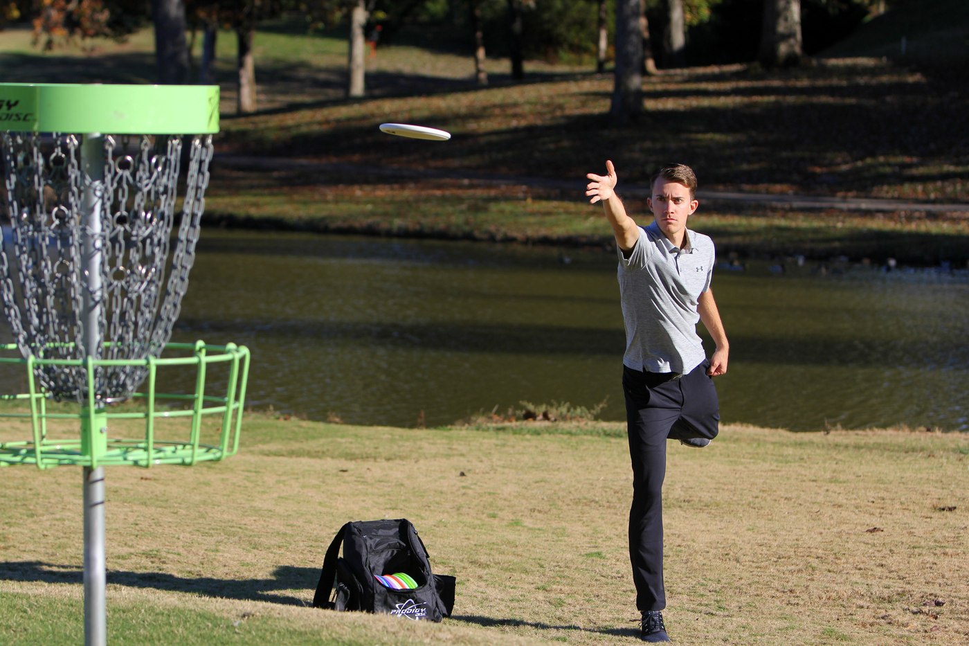 Will Schusterick following through on a throw, disc in flight beside a pond